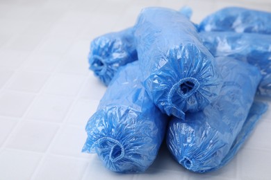 Rolled blue shoe covers on white tiled table, closeup. Space for text