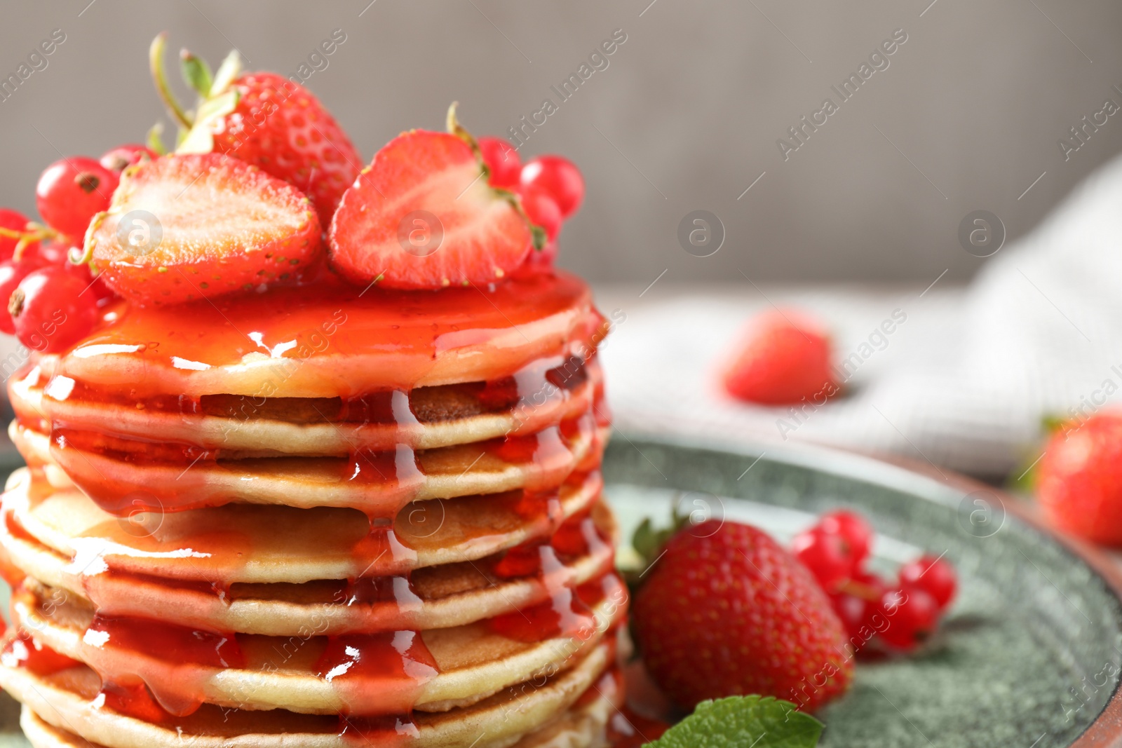 Photo of Delicious pancakes with fresh berries and syrup on table, closeup