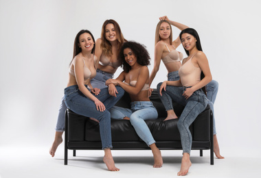 Group of women with different body types in jeans and underwear on sofa against light background