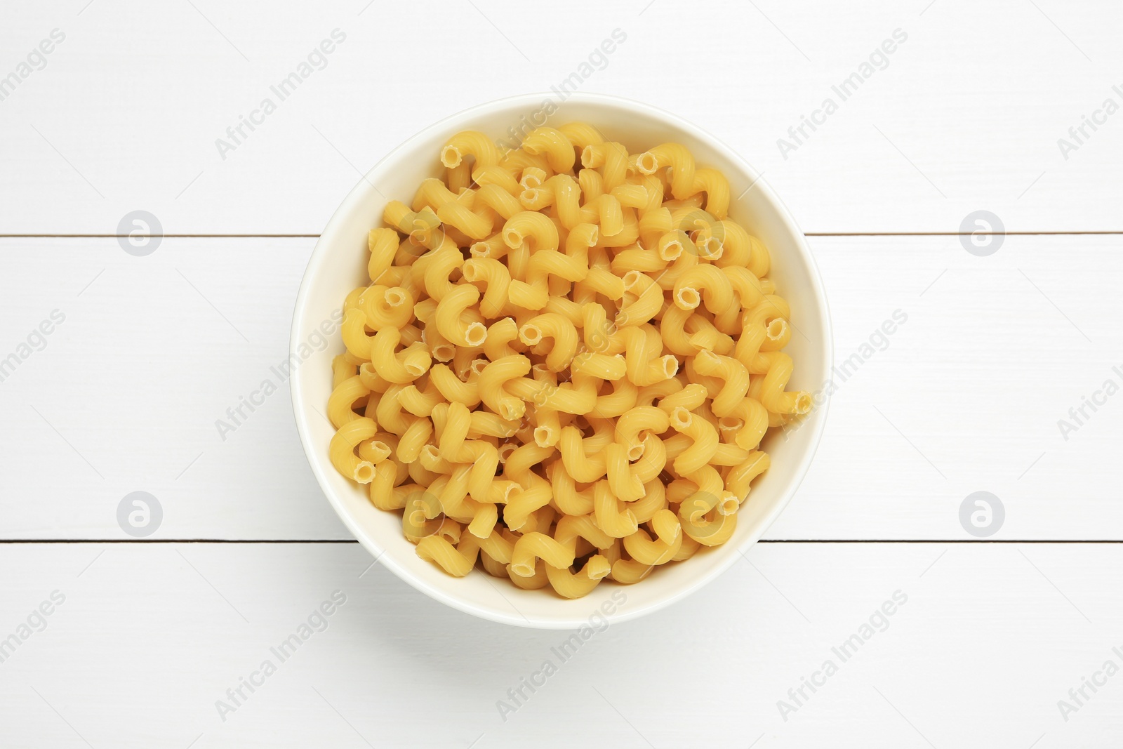Photo of Raw cavatappi pasta in bowl on white wooden table, top view