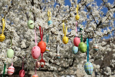 Photo of Beautifully painted Easter eggs hanging on blooming cherry tree outdoors