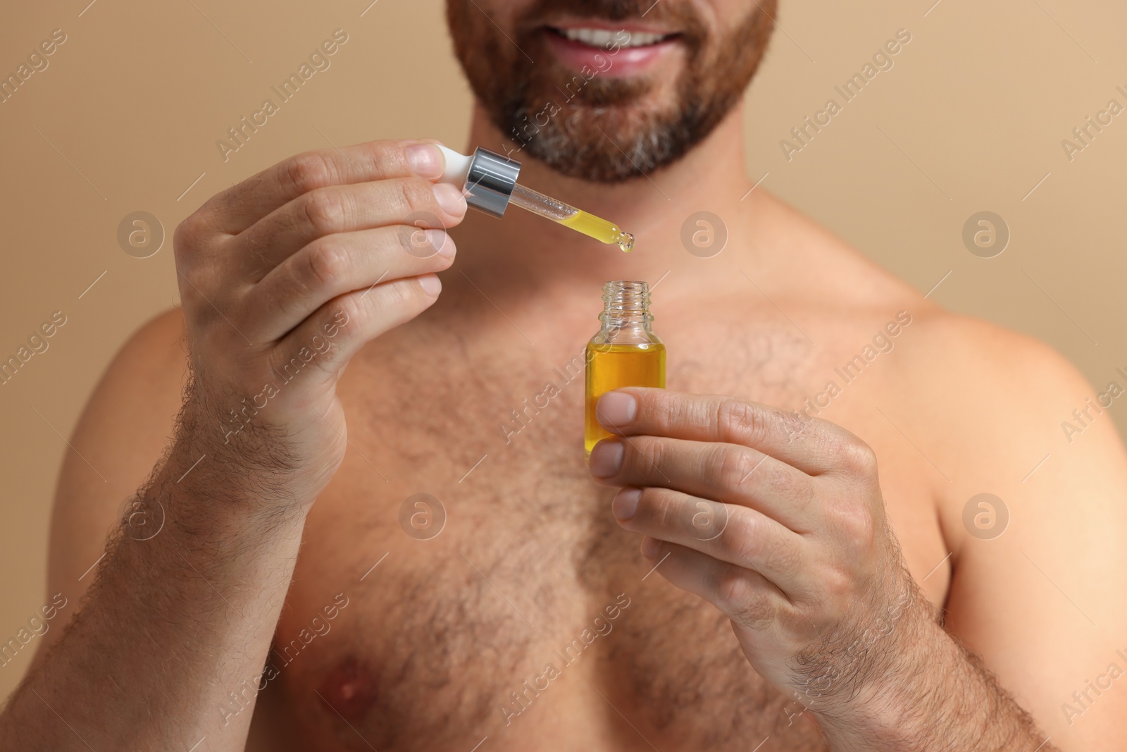 Photo of Smiling man with cosmetic serum on beige background, selective focus