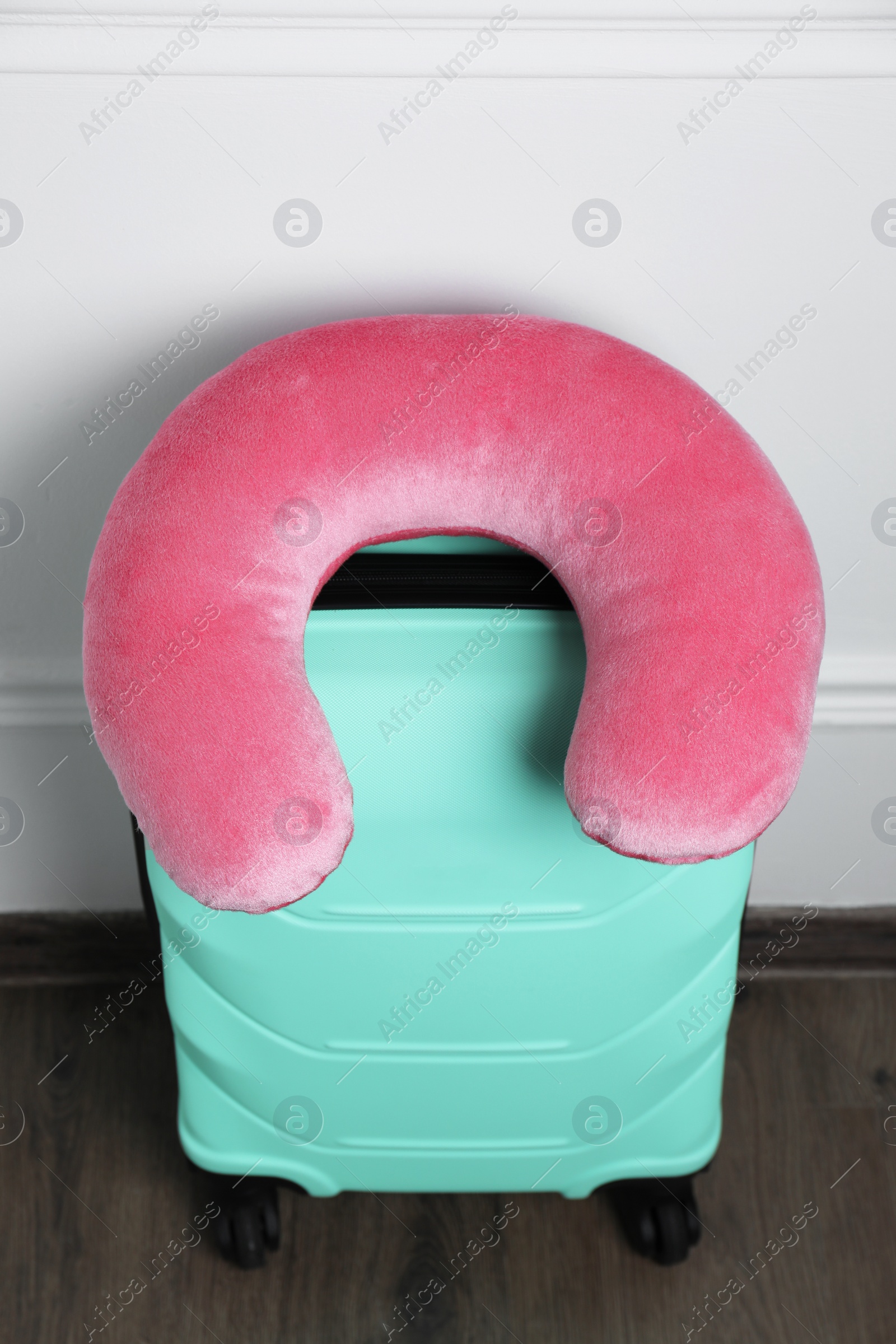 Photo of Pink travel pillow on turquoise suitcase indoors