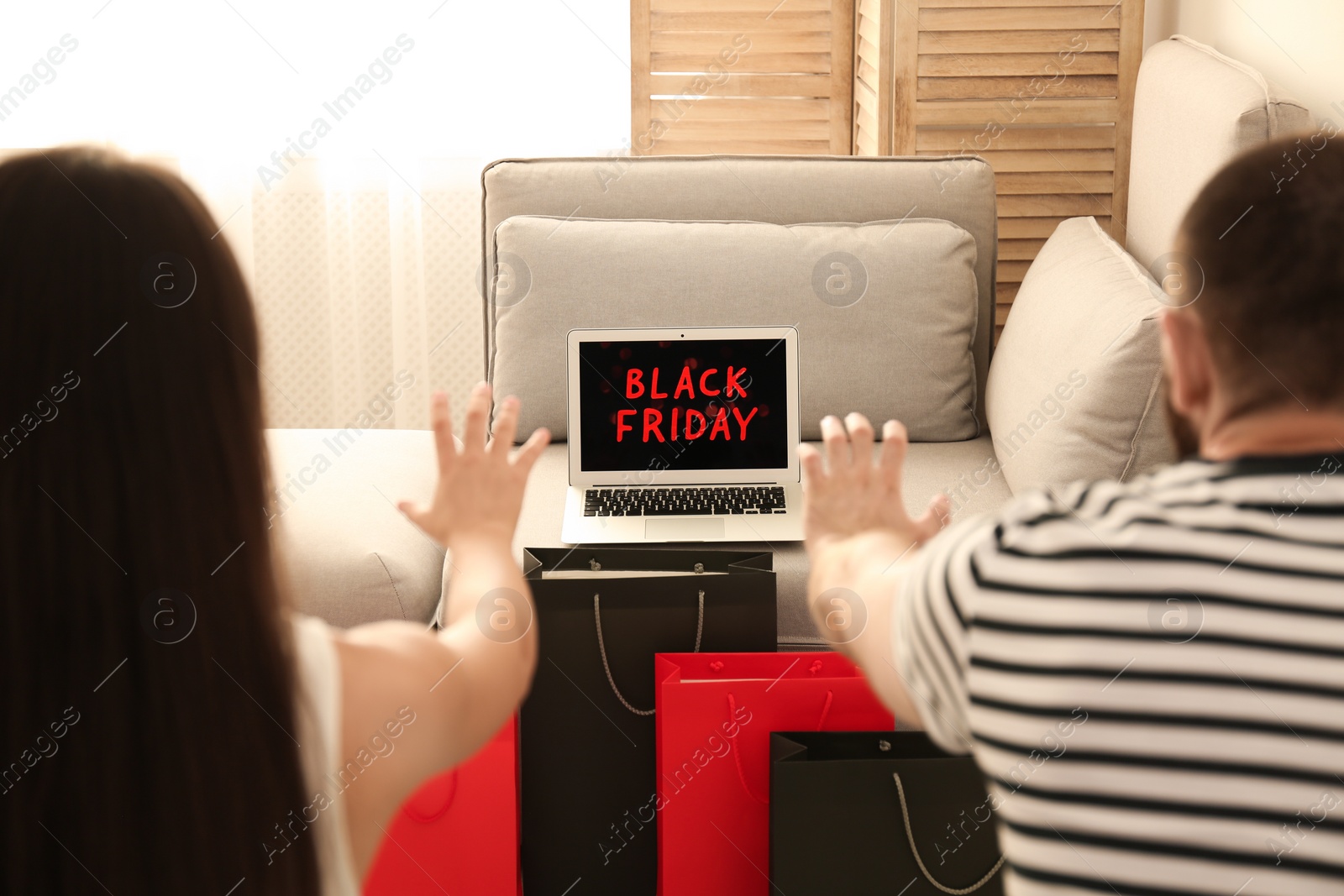 Photo of Couple reaching for laptop with Black Friday announcement on screen at home
