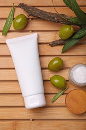 Tube of natural cream, olives and leaves on wooden table, flat lay