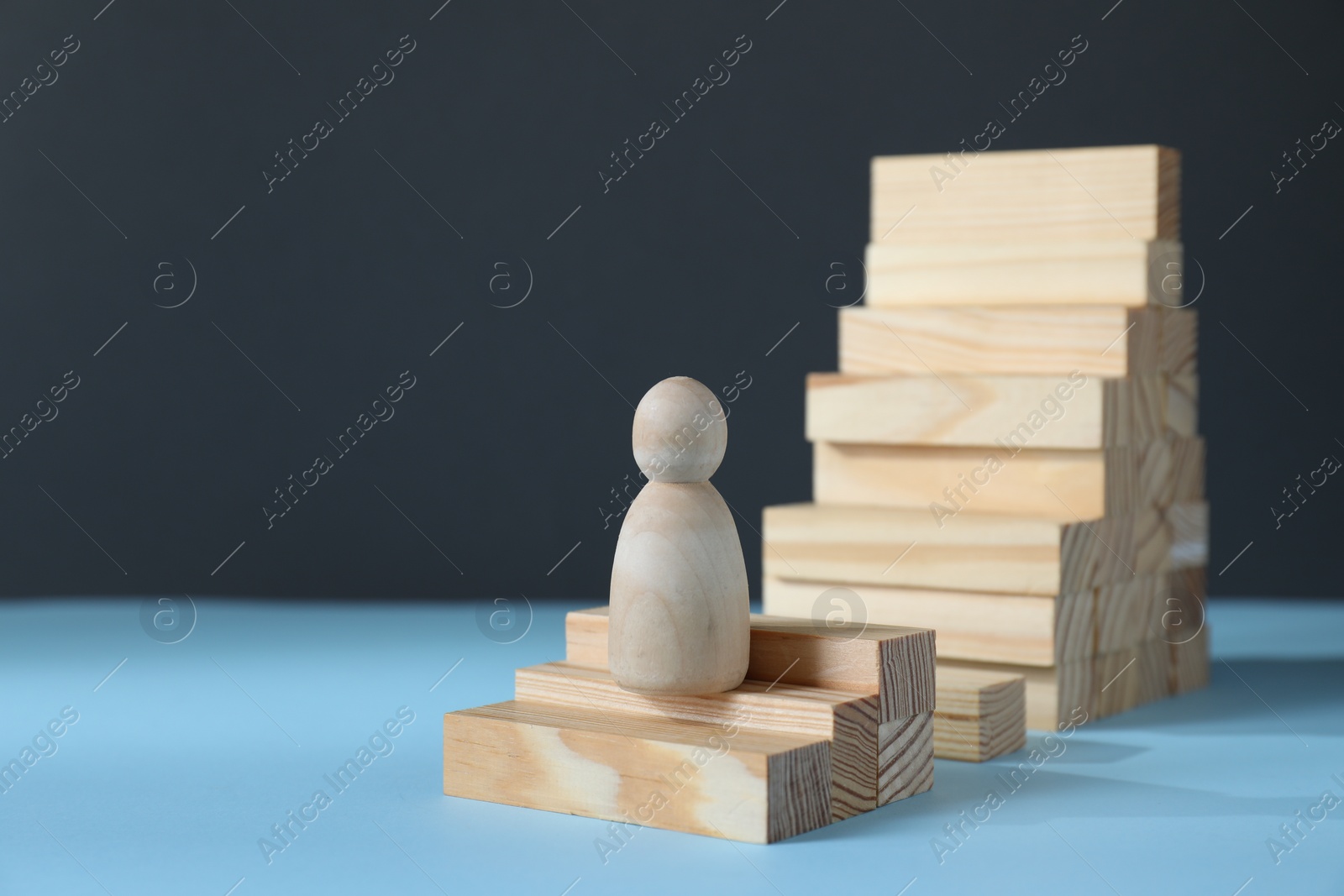Photo of Stairs of blocks with gap as barrier and wooden human figure on light blue surface, space. for text. Path to growth and success