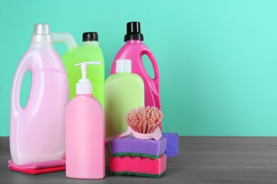 Photo of Different cleaning supplies and tools on wooden table against turquoise background, space for text