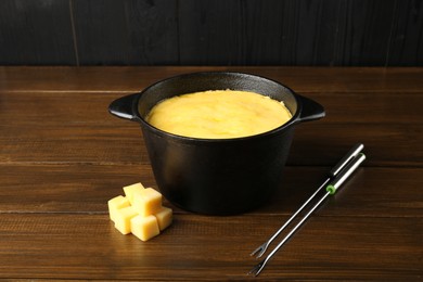 Photo of Fondue pot with melted cheese, forks and pieces at wooden table