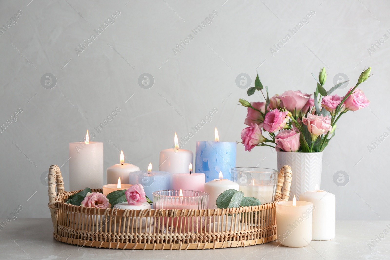 Photo of Composition with burning candles on table against light background