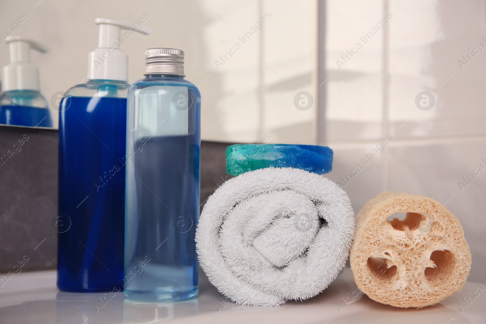 Photo of Loofah sponge, rolled towel and cosmetic products on sink in bathroom