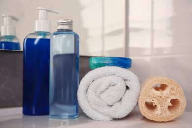 Loofah sponge, rolled towel and cosmetic products on sink in bathroom