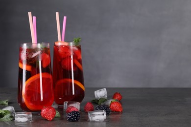 Delicious refreshing sangria, ice cubes and berries on grey table, space for text