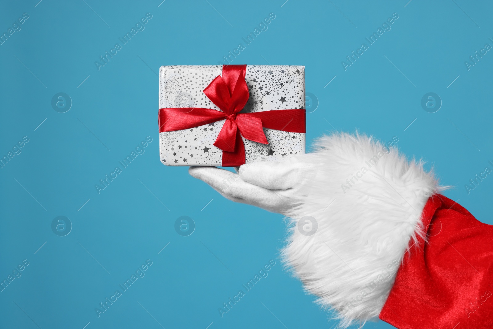 Photo of Santa Claus holding Christmas gift on light blue background, closeup