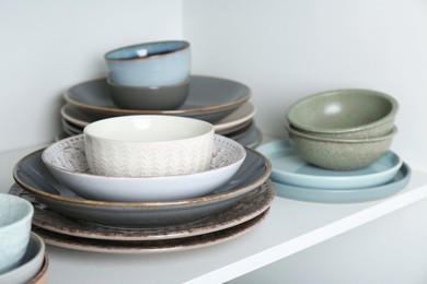 Photo of Different clean plates and bowls on shelf in cabinet, closeup
