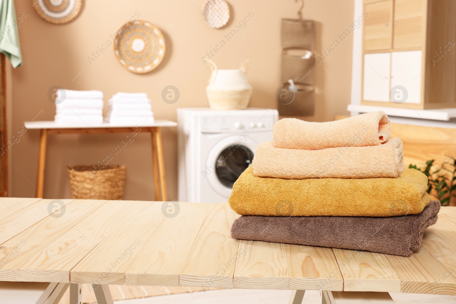 Photo of Stack of clean towels on wooden table in laundry room, space for text