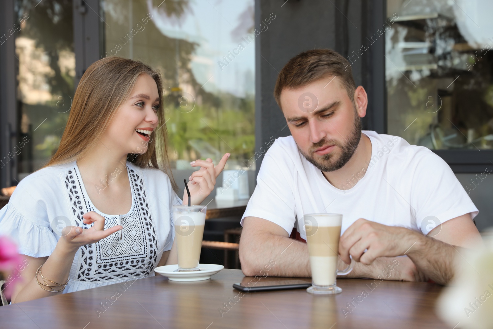 Photo of Young man having boring date with talkative girl in outdoor cafe