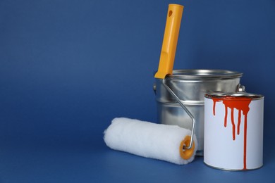 Photo of Cans of orange paint and brush roller on blue background. Space for text
