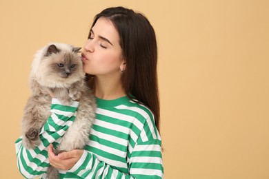 Photo of Woman kissing her cute cat on light brown background, space for text