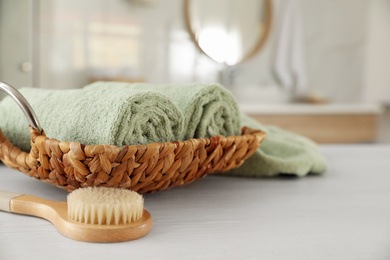 Photo of Wicker basket with rolled towels and massage brush on white wooden table in bathroom