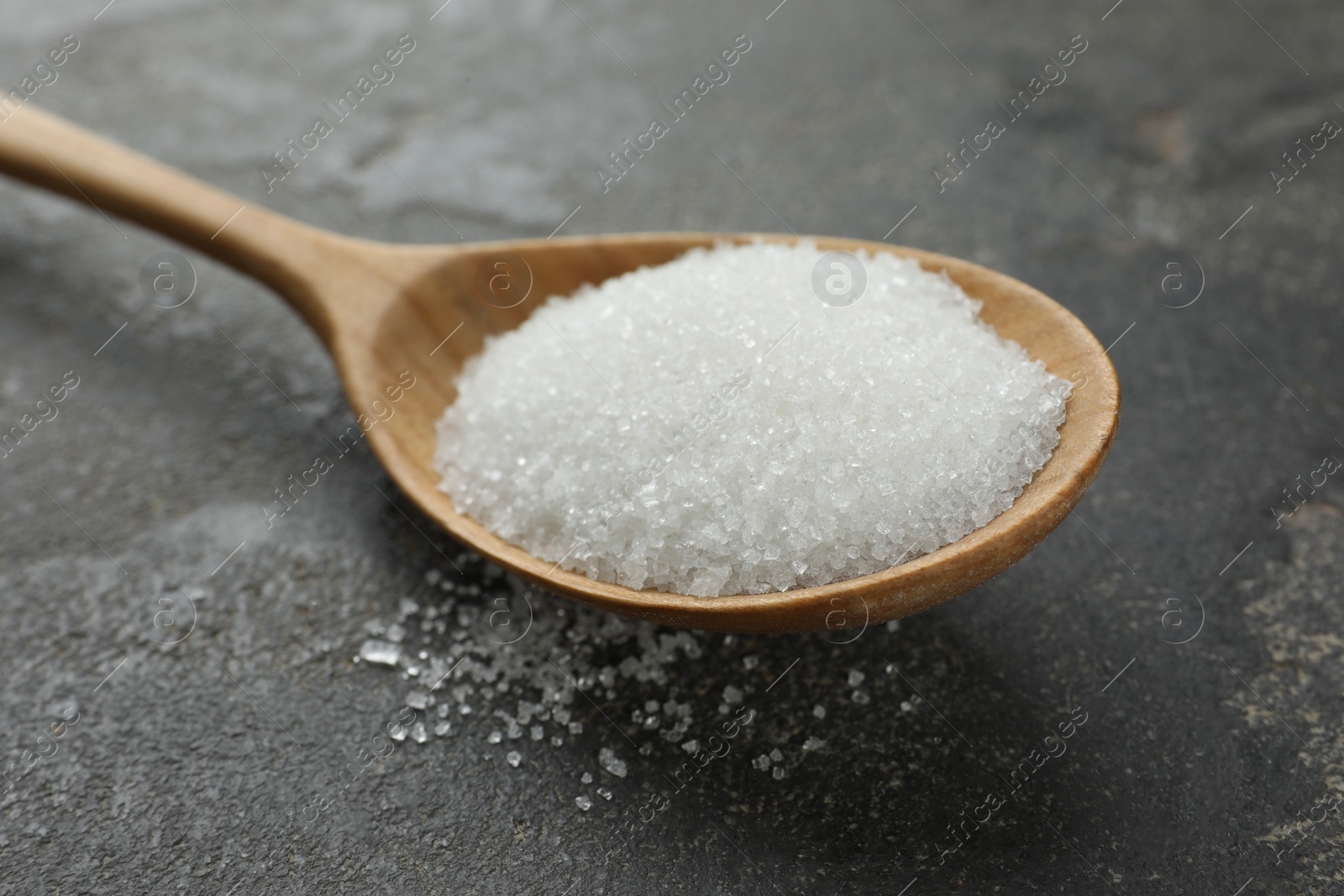 Photo of Spoon with granulated sugar on grey textured table, closeup