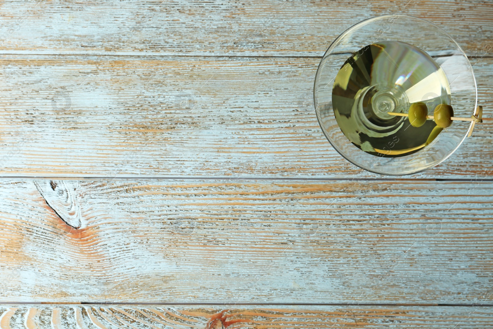 Photo of Glass of Classic Dry Martini with olives on wooden table, top view. Space for text