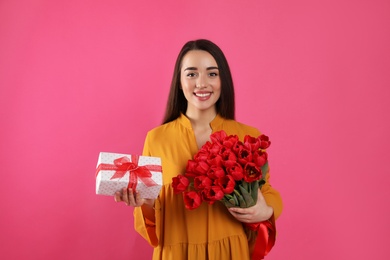 Photo of Happy woman with red tulip bouquet and gift box on pink background. 8th of March celebration