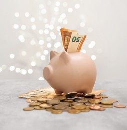 Photo of Piggy bank with euro banknote and coins on grey table against blurred lights, space for text