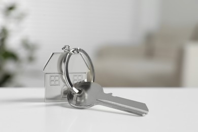 Photo of Key with keychain in shapehouse on white table against blurred background, closeup. Space for text