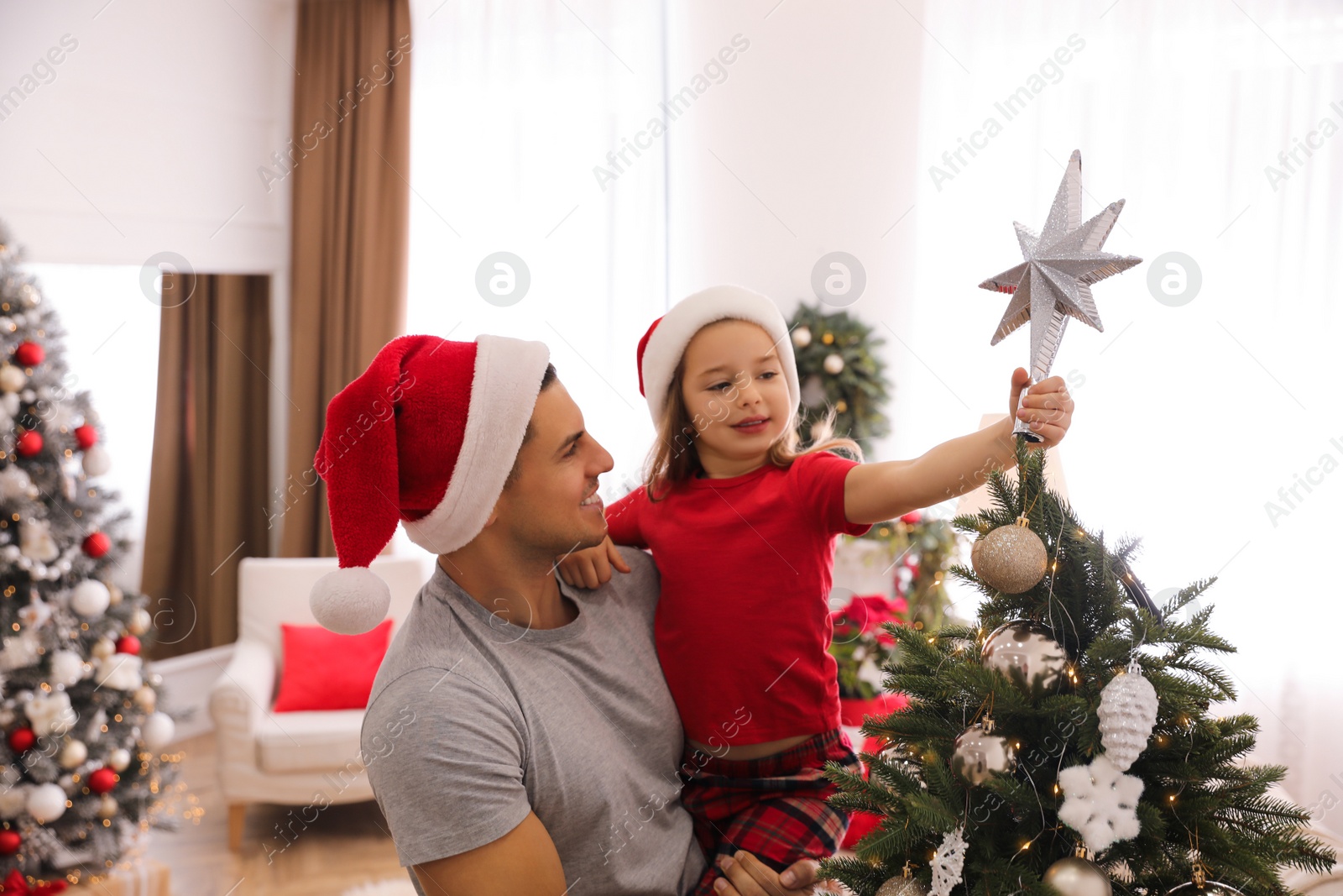 Photo of Father and little daughter decorating Christmas tree with star topper indoors