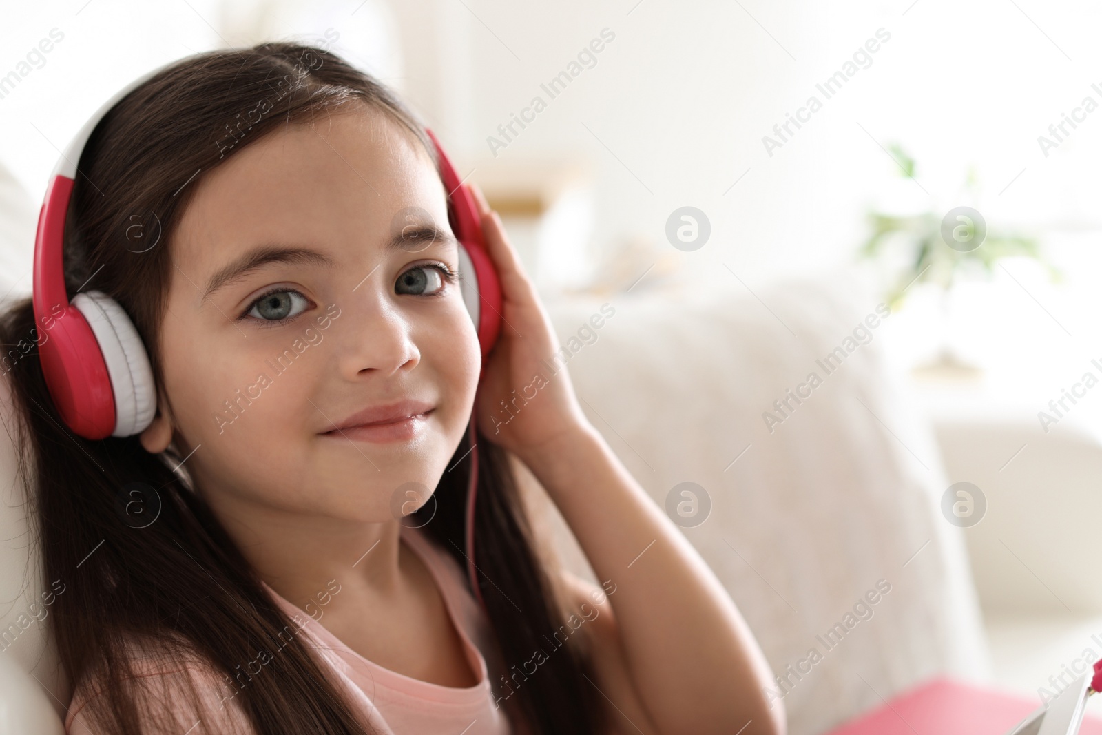 Photo of Cute little girl with headphones listening to audiobook at home