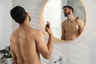 Man spraying luxury perfume near mirror indoors
