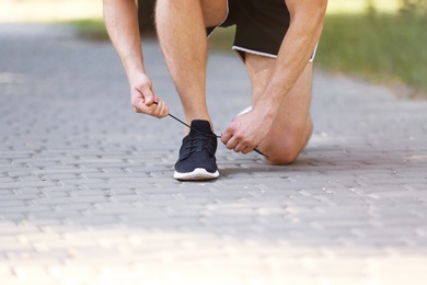 Photo of Young man tying shoelaces before running outdoors, focus on legs