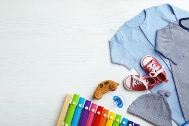 Flat lay composition with cute clothes and space for text on white wooden background. Baby accessories