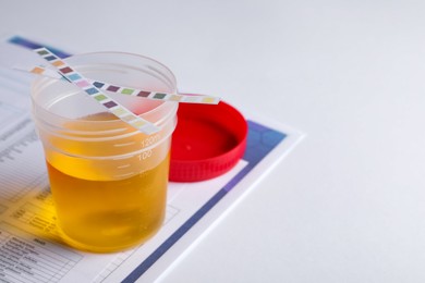 Container with urine sample for analysis and test strips on white table, closeup. Space for text
