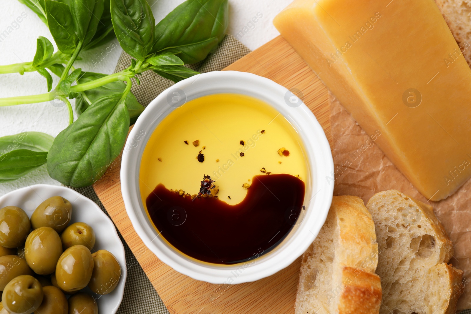Photo of Bowl of organic balsamic vinegar with oil, basil, bread, cheese and olives on table, flat lay
