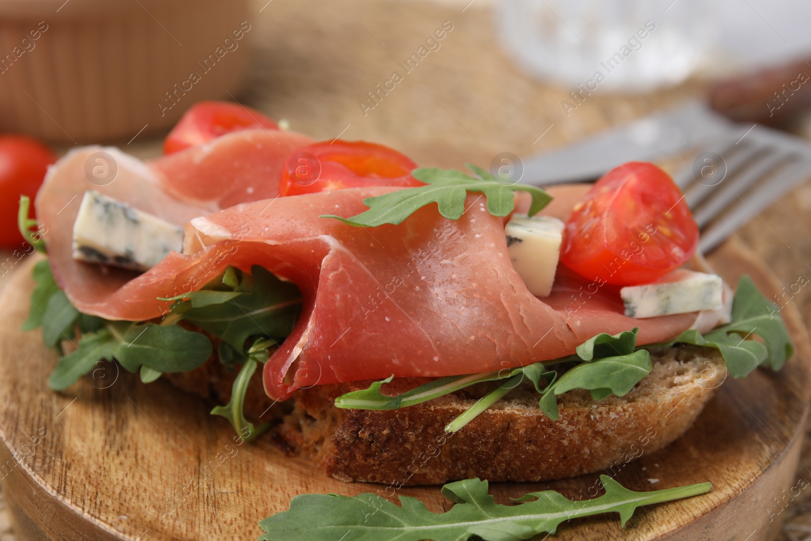 Photo of Tasty bruschetta with prosciutto, arugula, cheese and tomato on wooden board, closeup