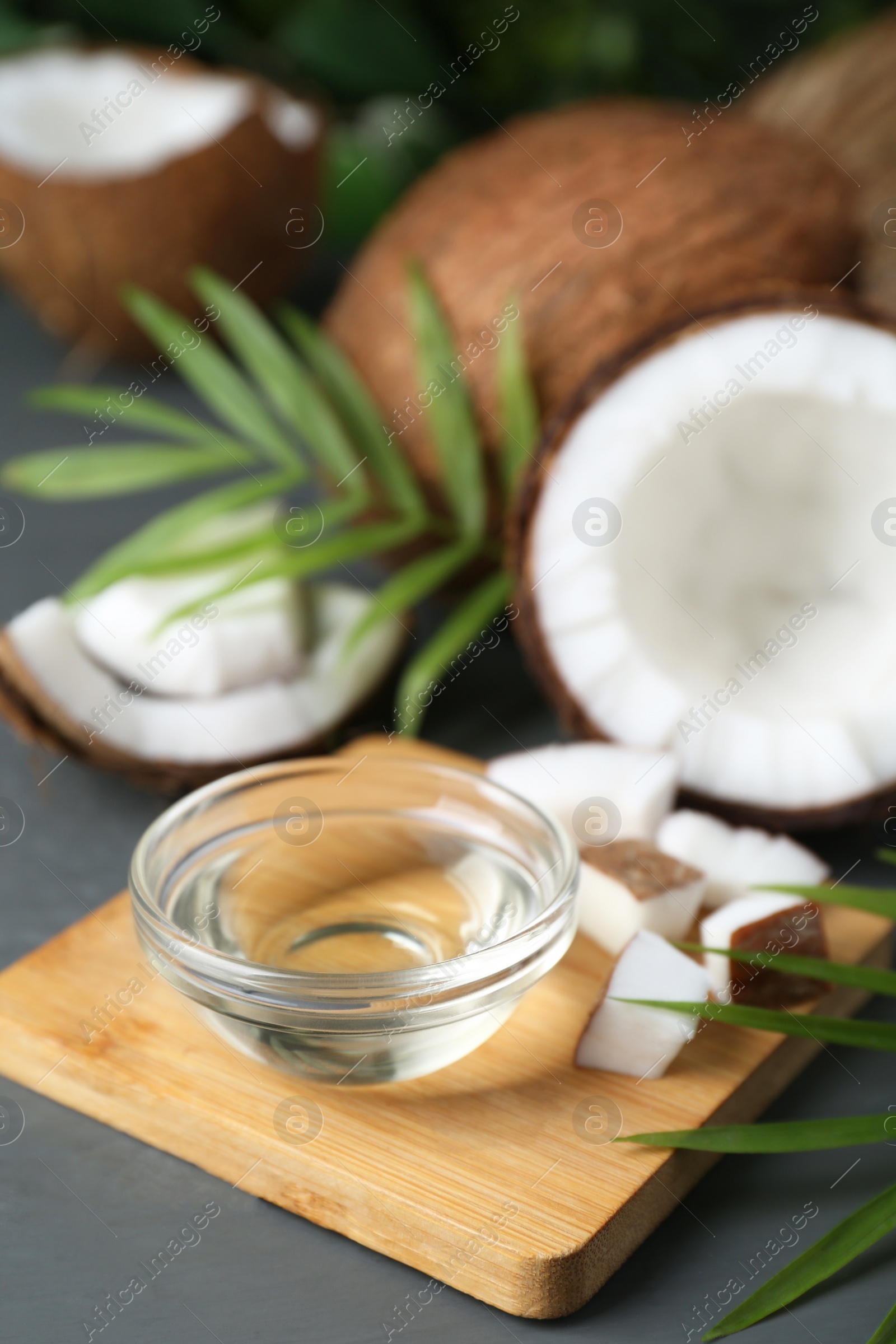 Photo of Organic coconut cooking oil, leaves and fresh fruits on grey table