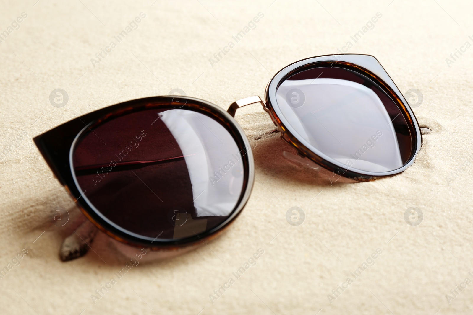 Photo of Stylish sunglasses on white sand. Summer time