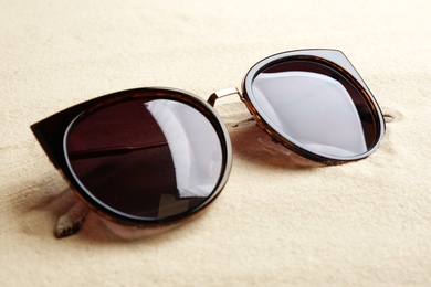 Photo of Stylish sunglasses on white sand. Summer time