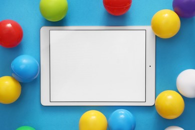 Photo of Modern tablet and balls on light blue background, flat lay. Space for text