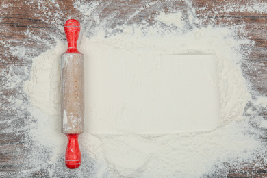 Photo of Flour and rolling pin on wooden table, top view. Space for text