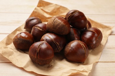 Photo of Roasted edible sweet chestnuts on wooden table, closeup