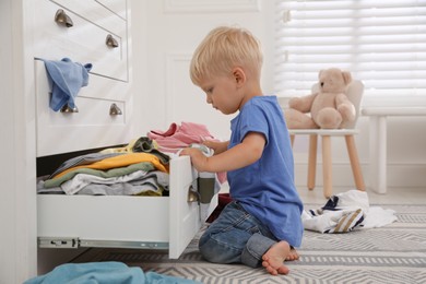 Cute little boy playing with clothes in dresser's drawer at home