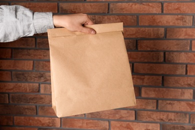 Photo of Woman holding paper bag against brick wall. Mockup for design