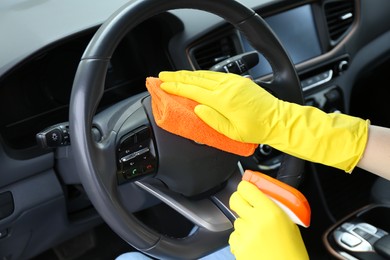 Photo of Woman cleaning steering wheel with rag in car, closeup