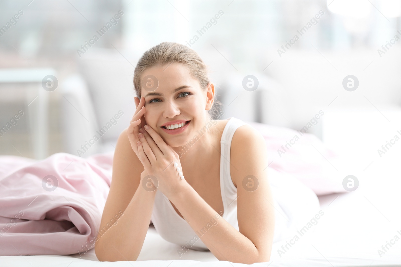 Photo of Young woman applying hand cream on bed at home