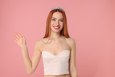 Beautiful young woman with tiara on pink background