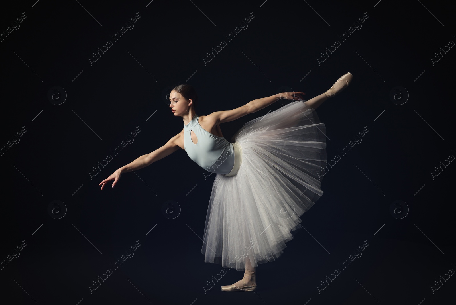 Photo of Young ballerina practicing dance moves on black background