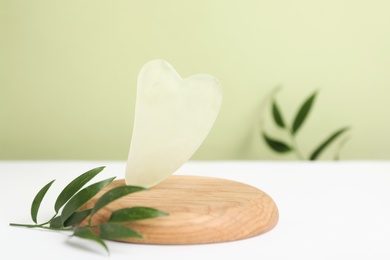 Photo of Jade gua sha tool  and green leaf on white table