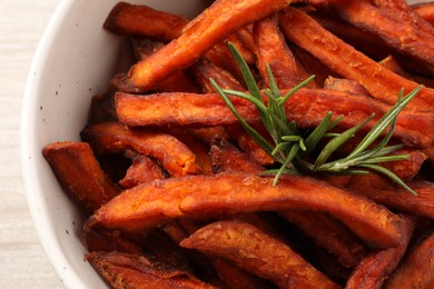 Photo of Sweet tasty potato fries and rosemary in bowl, top view